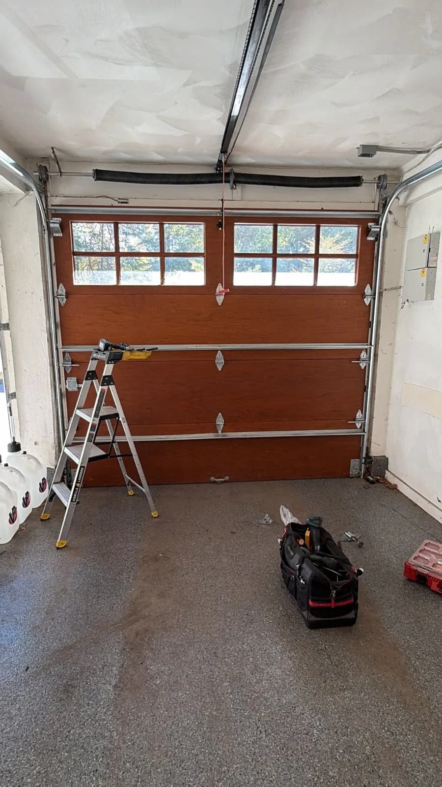 Interior view of a closed wood-finish garage door with top windows, a stepladder, and a tool bag on the floor in Avon, CT.